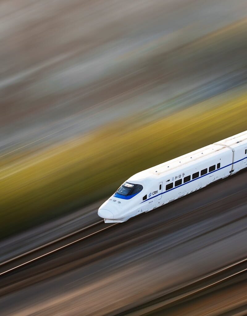 A sleek white high-speed train traveling at top speed, captured with a motion blur effect.