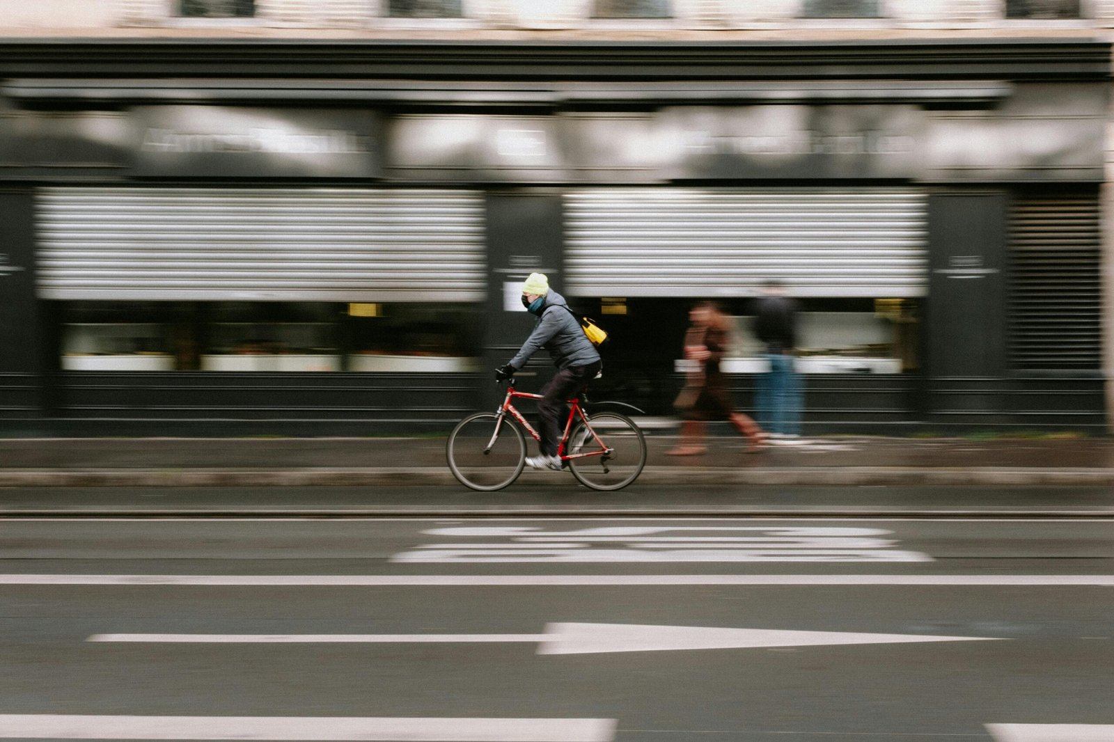 Blurry cyclist in winter jacket biking swiftly on a city street showcasing motion blur.