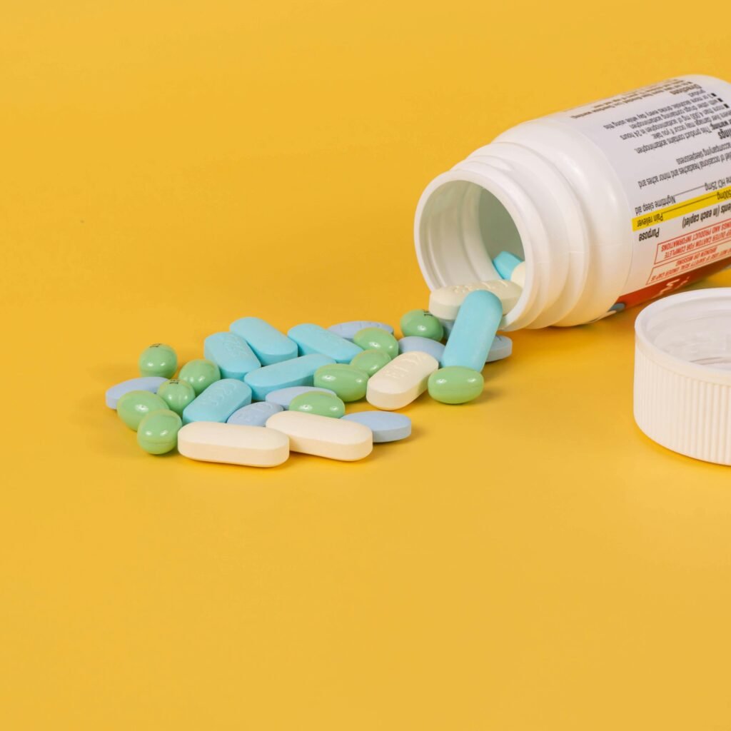 Various pills spill from a bottle onto a vibrant yellow surface, highlighting health themes.