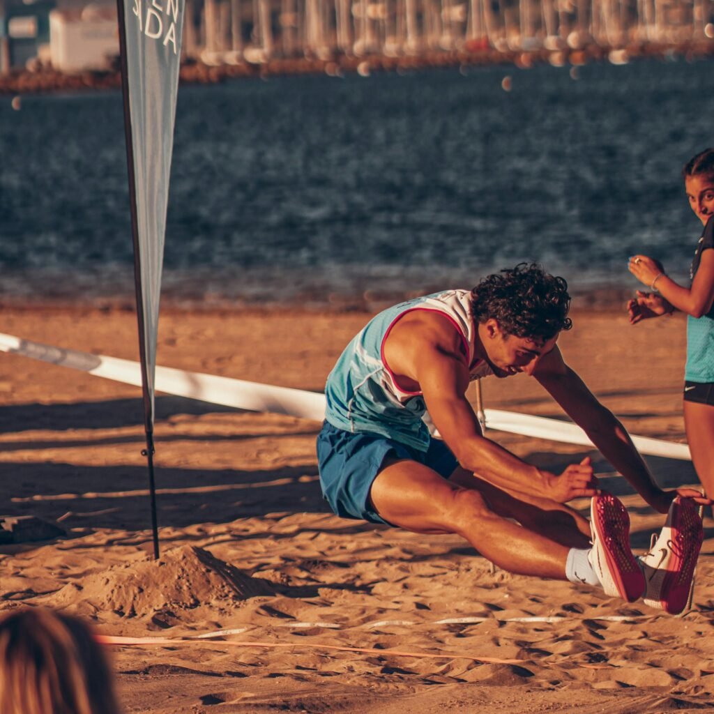 Athletes perform long jump on the beach in Sada, Spain, capturing energetic action in the sun.