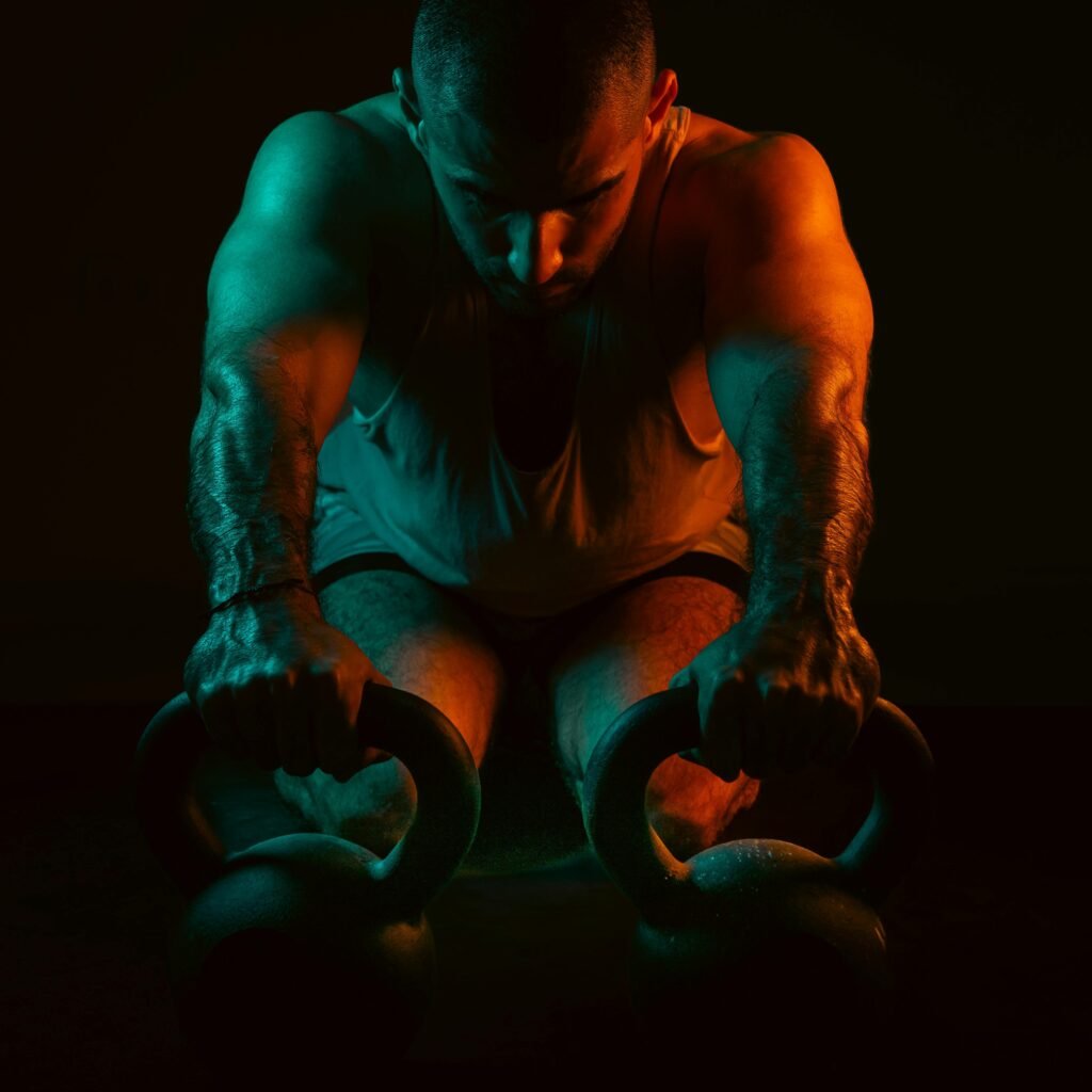 A strong man intensely working out with kettlebells in a dark gym setting.