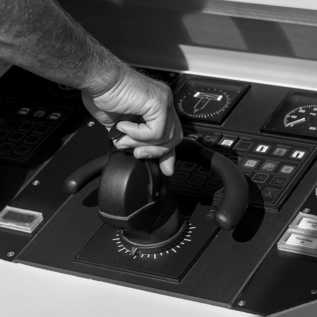 Black and white image of a person's hand adjusting a throttle lever on a boat control panel.