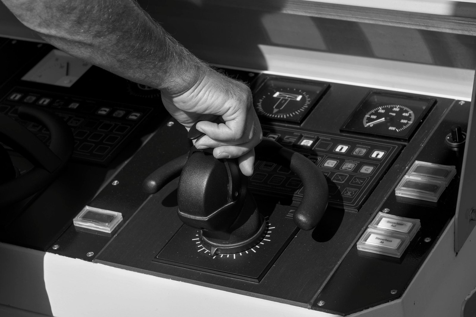 Black and white image of a person's hand adjusting a throttle lever on a boat control panel.