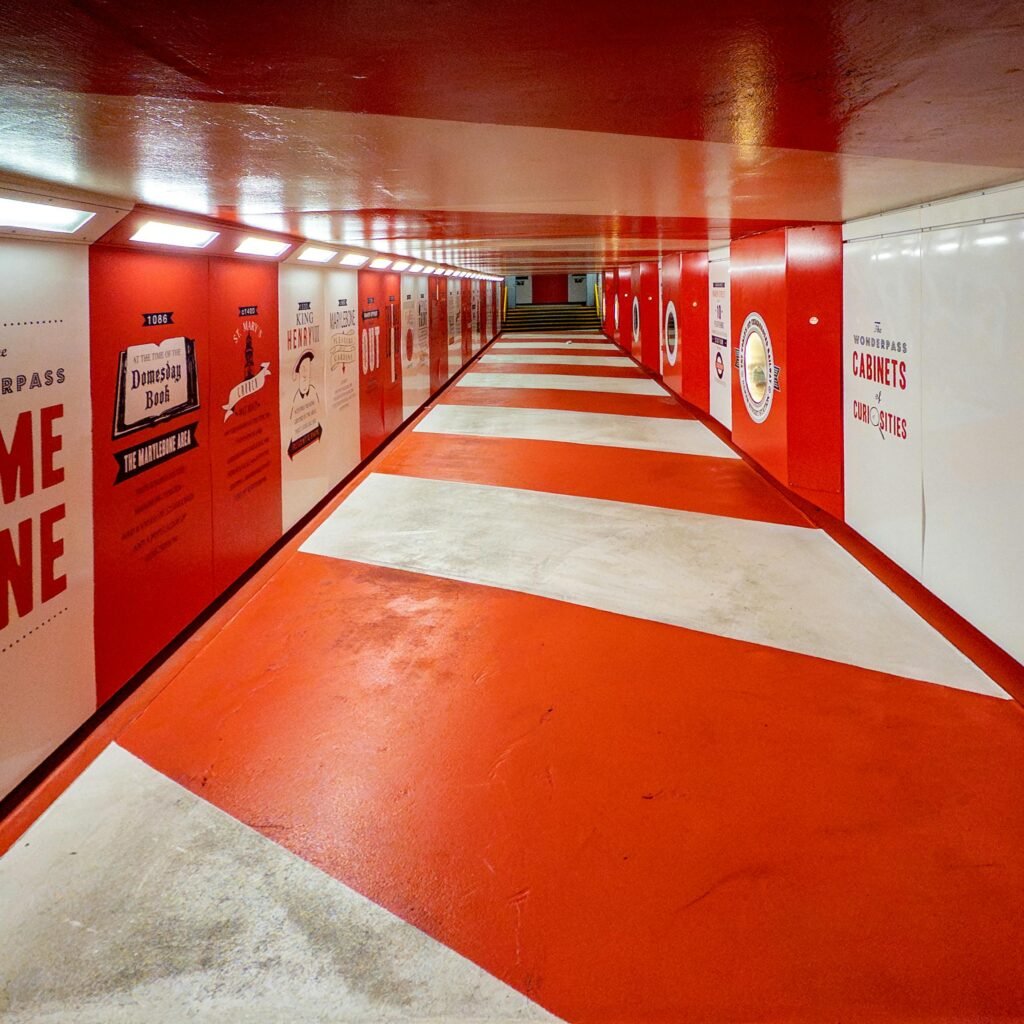 Brightly lit red and white tunnel in London showcasing vibrant artwork and signs.