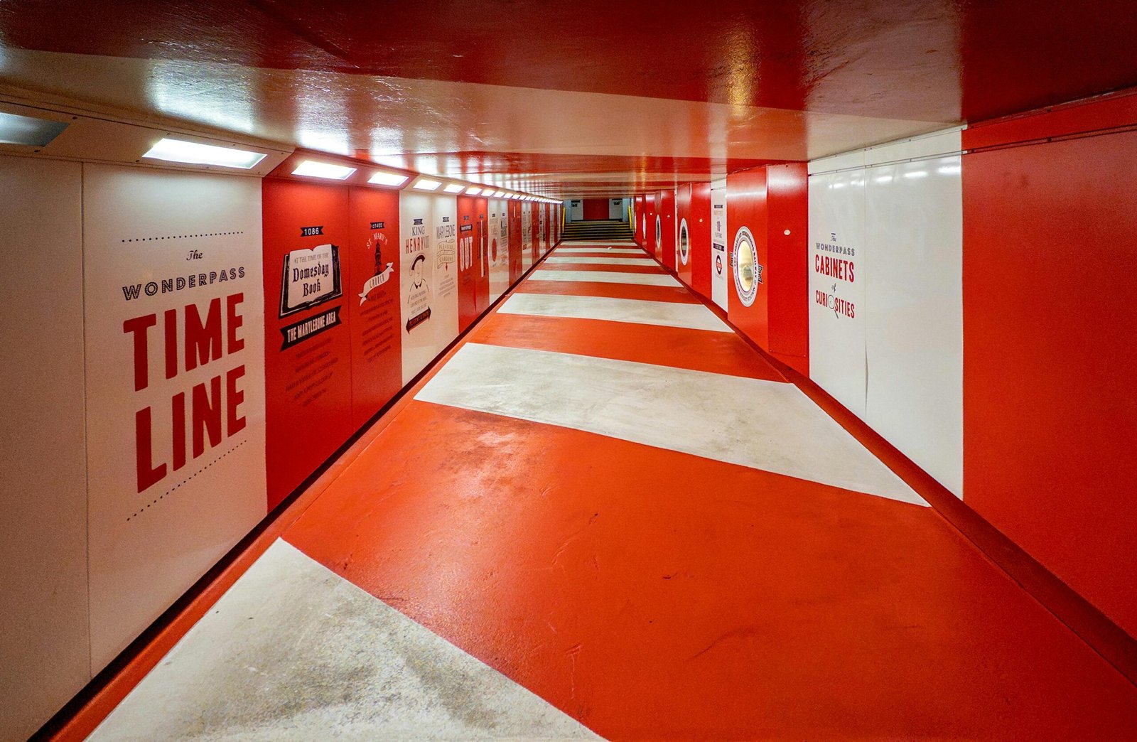 Brightly lit red and white tunnel in London showcasing vibrant artwork and signs.
