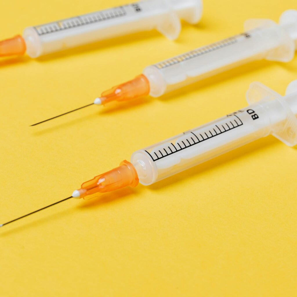 Plastic empty medical syringe injectors with orange needle hubs and without protective cover placed on bright yellow surface