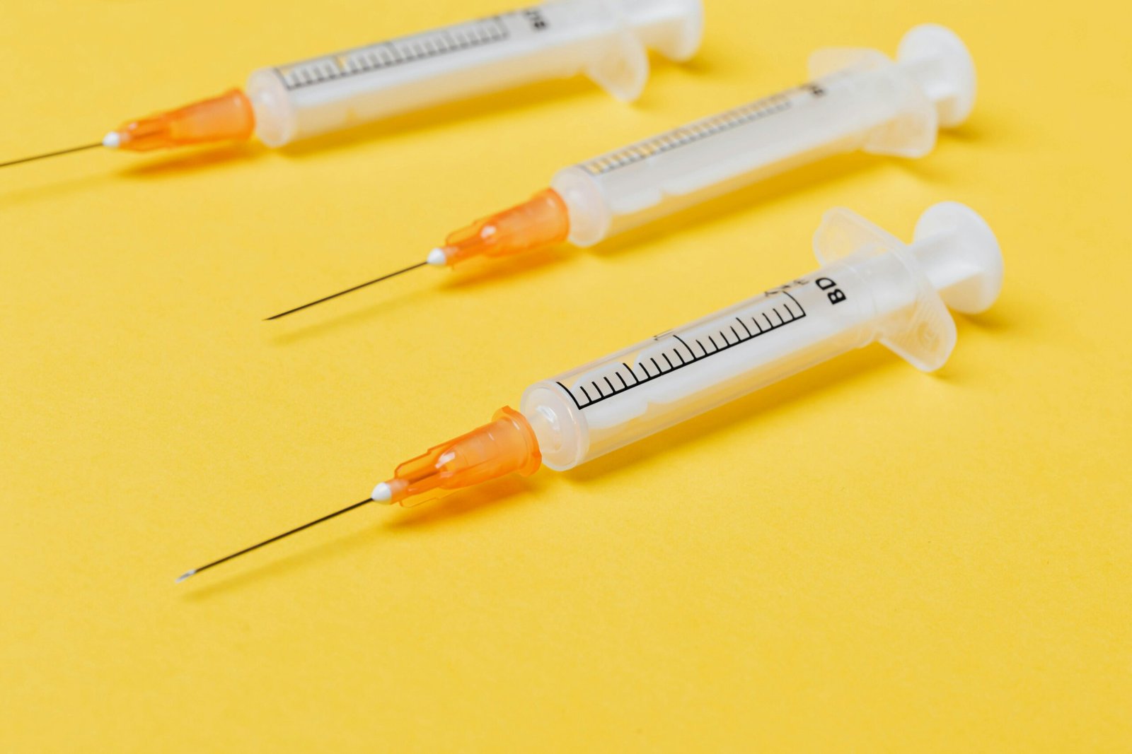 Plastic empty medical syringe injectors with orange needle hubs and without protective cover placed on bright yellow surface