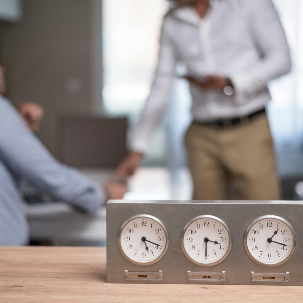 Two businessmen in an office with clocks showing different time zones, symbolizing global business.