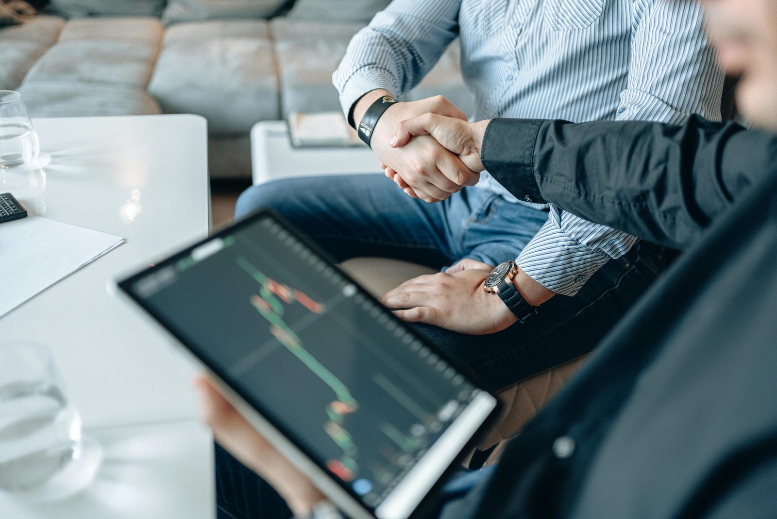 Two businesspeople shaking hands over stock market data on a tablet.