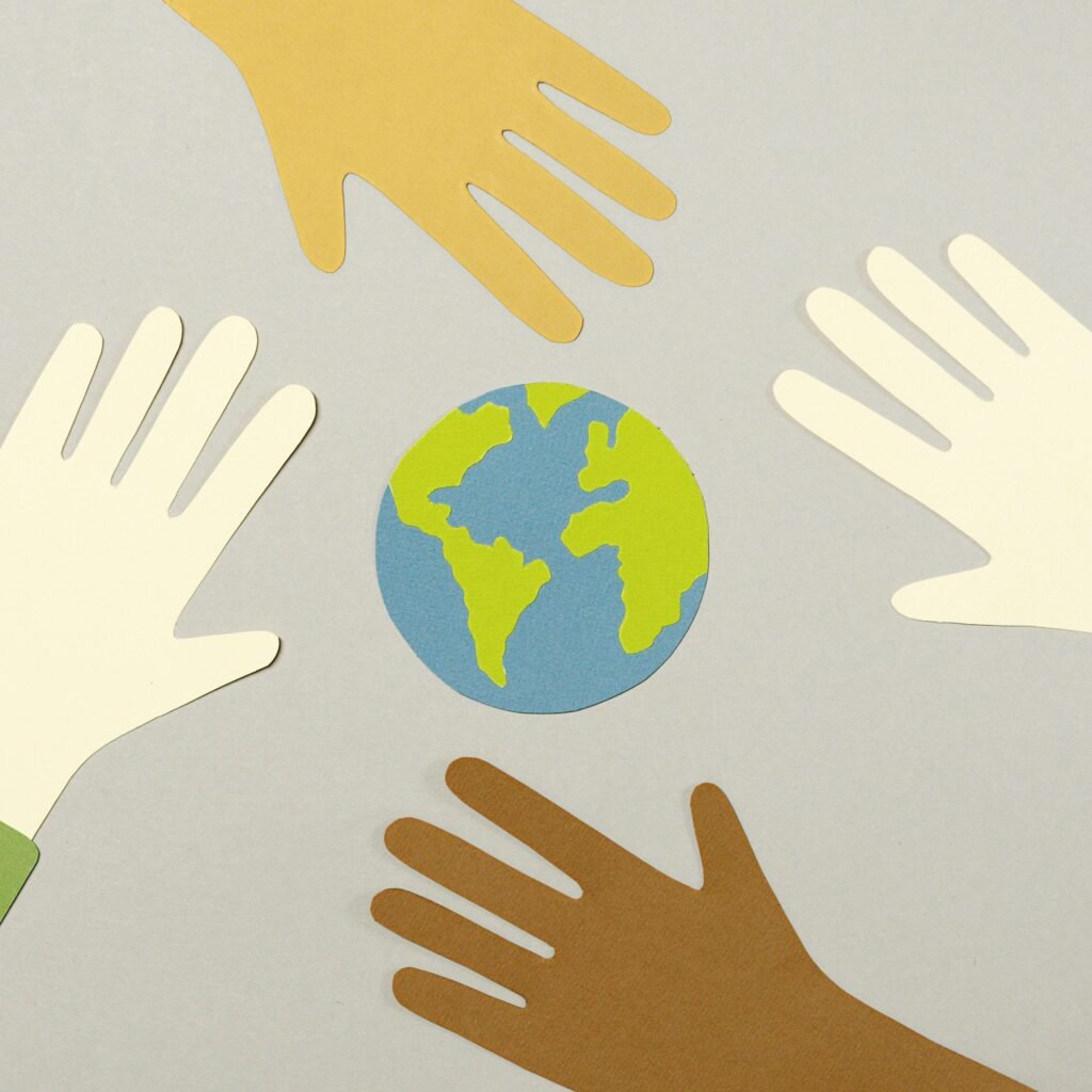 Colorful paper cutouts of diverse hands surrounding a small paper Earth, symbolizing unity.