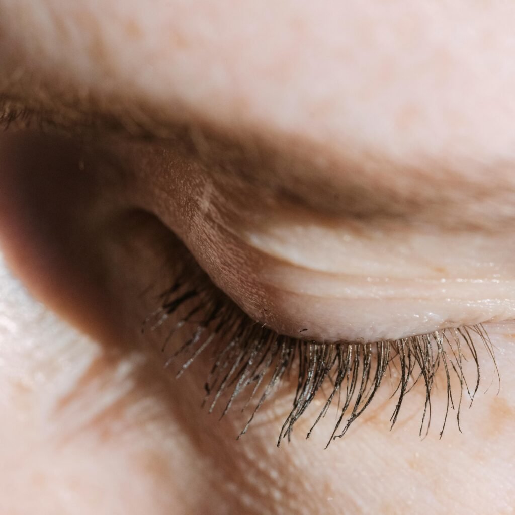Closeup of crop unrecognizable female with closed eye and long eyelashes with eyebrow standing in light room with sunlight at home