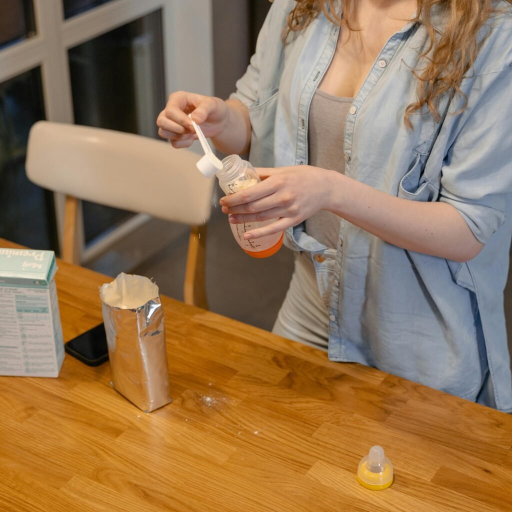 A woman prepares baby formula in a modern kitchen, captured during a daytime routine.