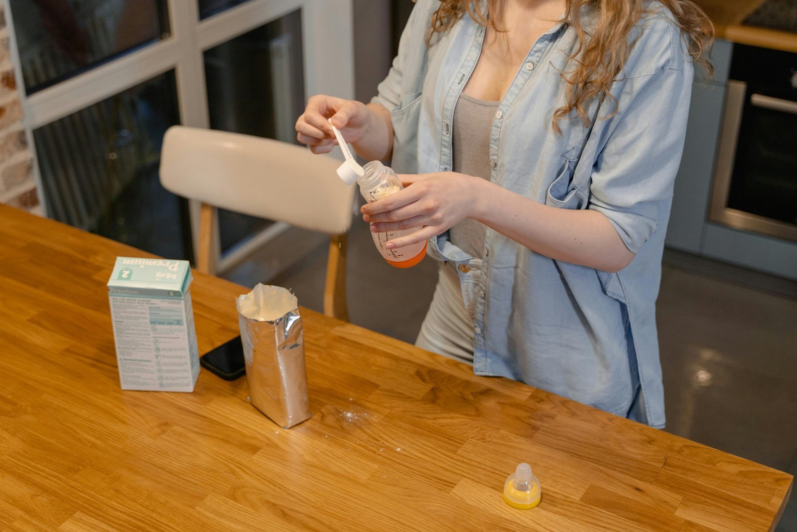 A woman prepares baby formula in a modern kitchen, captured during a daytime routine.
