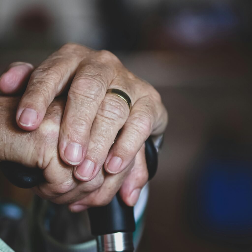 Close-up of senior hands clasped around a cane, highlighting a wedding ring, symbolizing love and support.