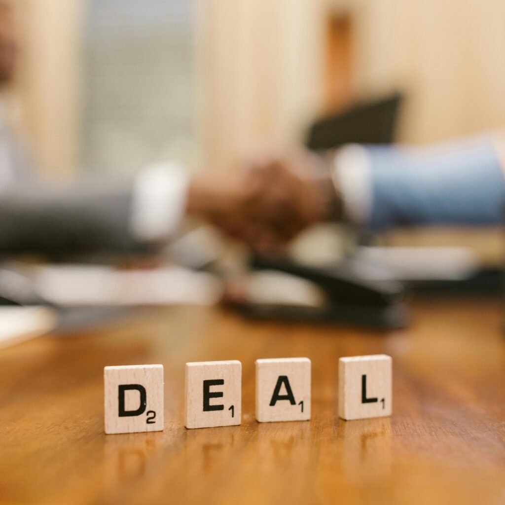Close-up of Scrabble tiles spelling 'deal' with a handshake in the background.
