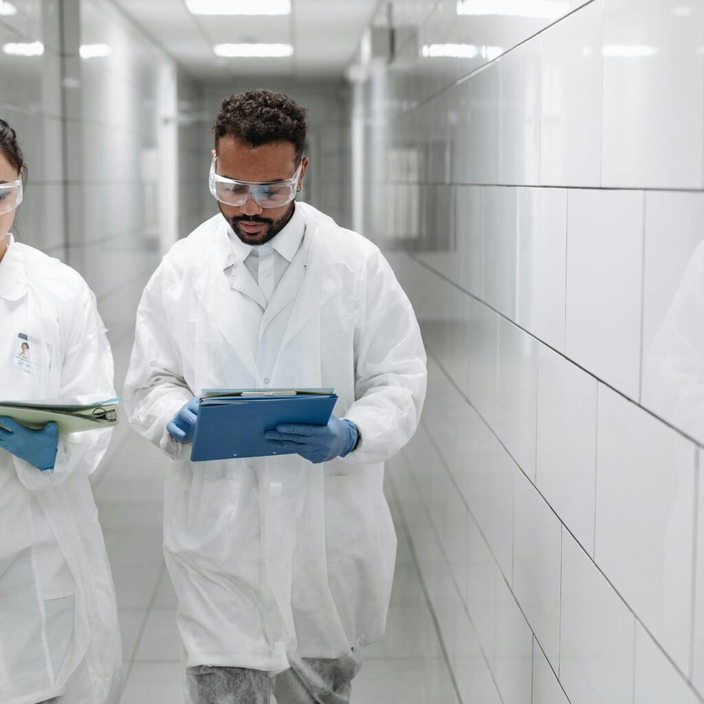 Two researchers in lab coats review documents in a clinical laboratory hallway.
