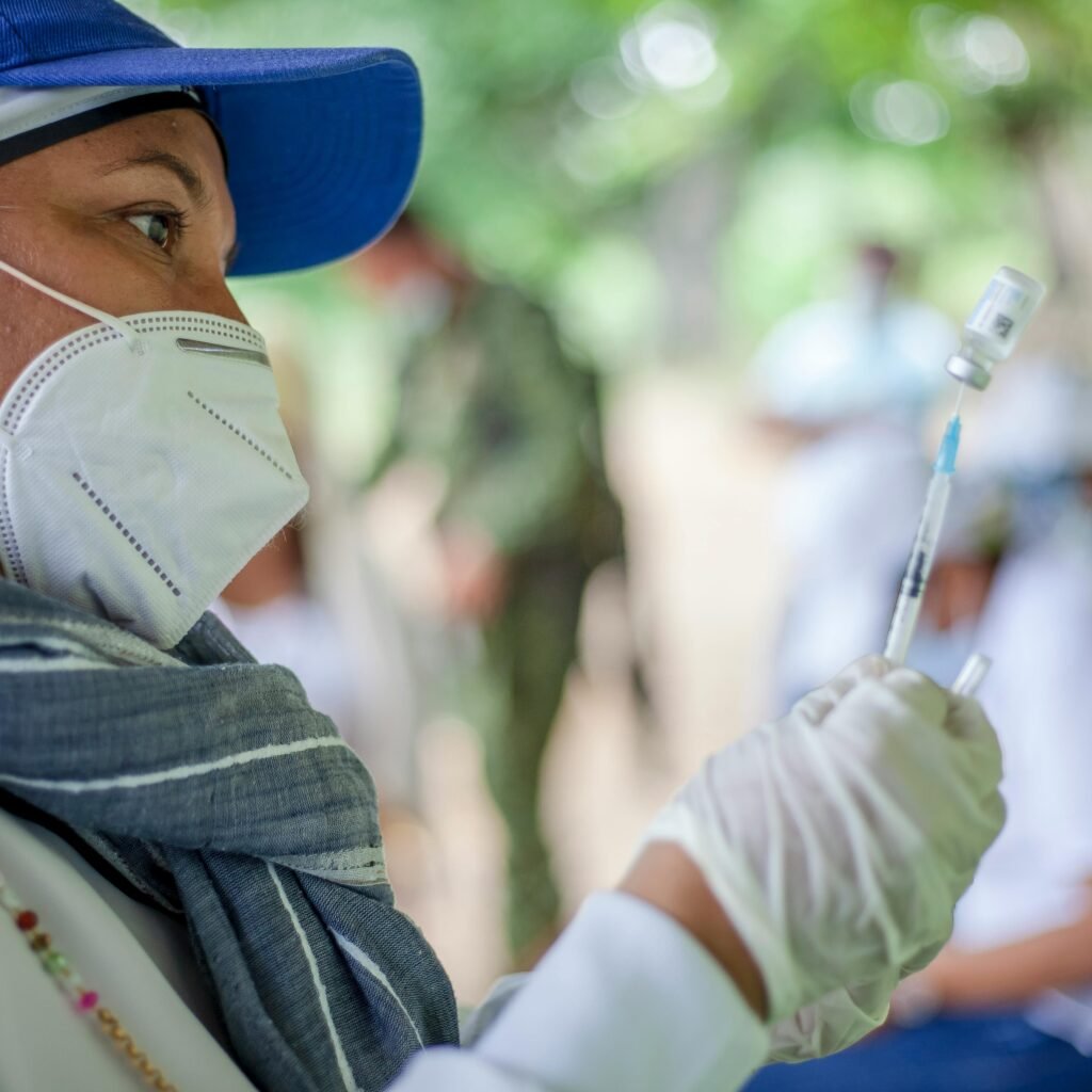 A healthcare worker prepares a vaccine outdoors in Ovejas, Colombia, emphasizing COVID-19 safety and healthcare provision.