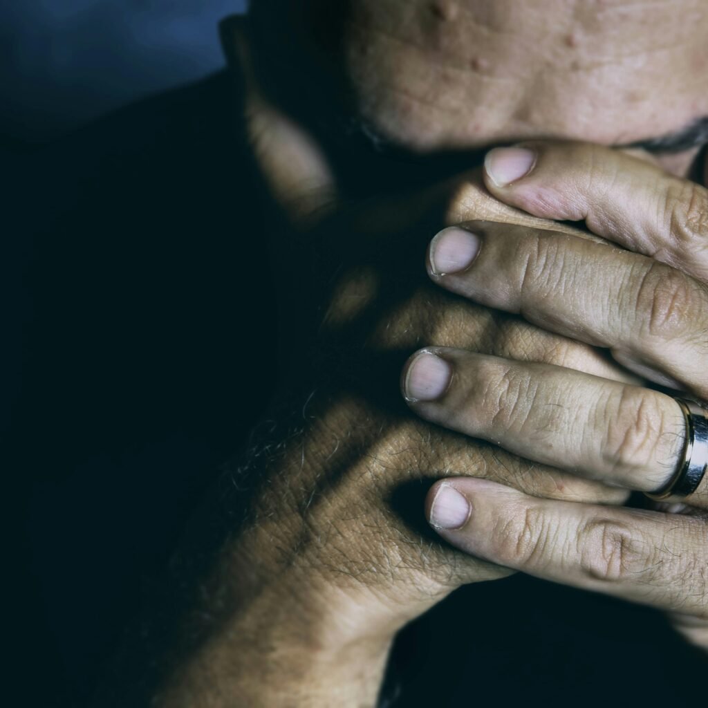 Close-up of an elderly man covering his face, expressing sadness and contemplation.