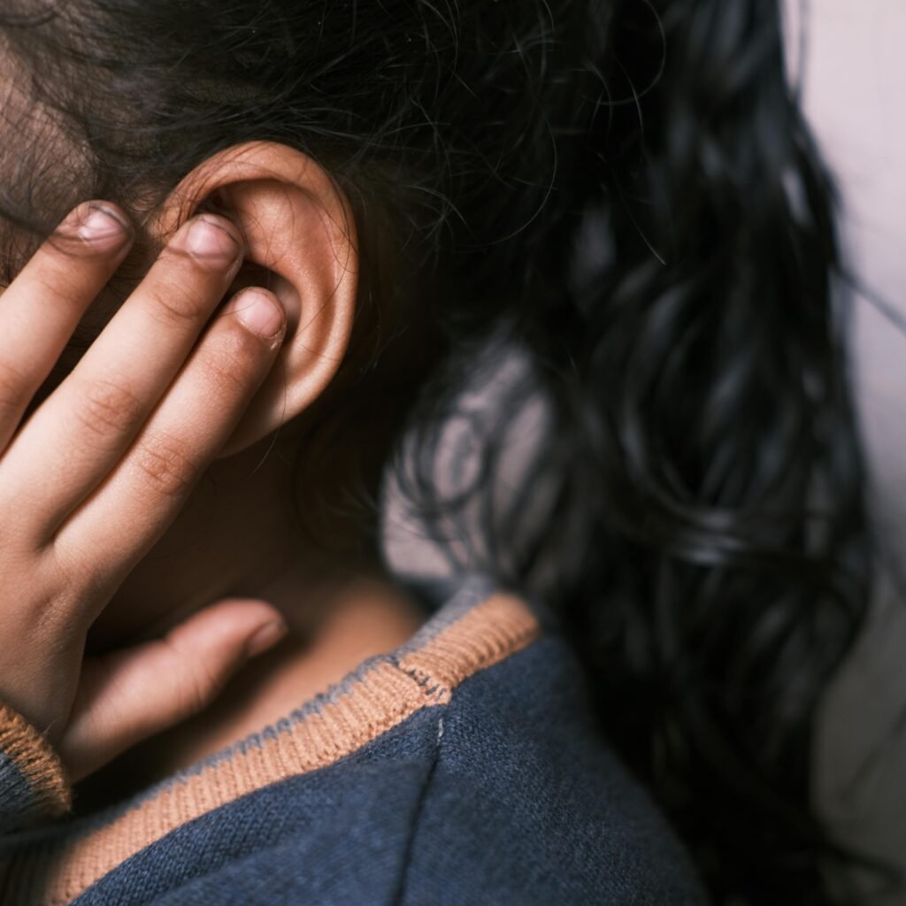 A young girl with long dark hair covering her ear in a thoughtful pose.