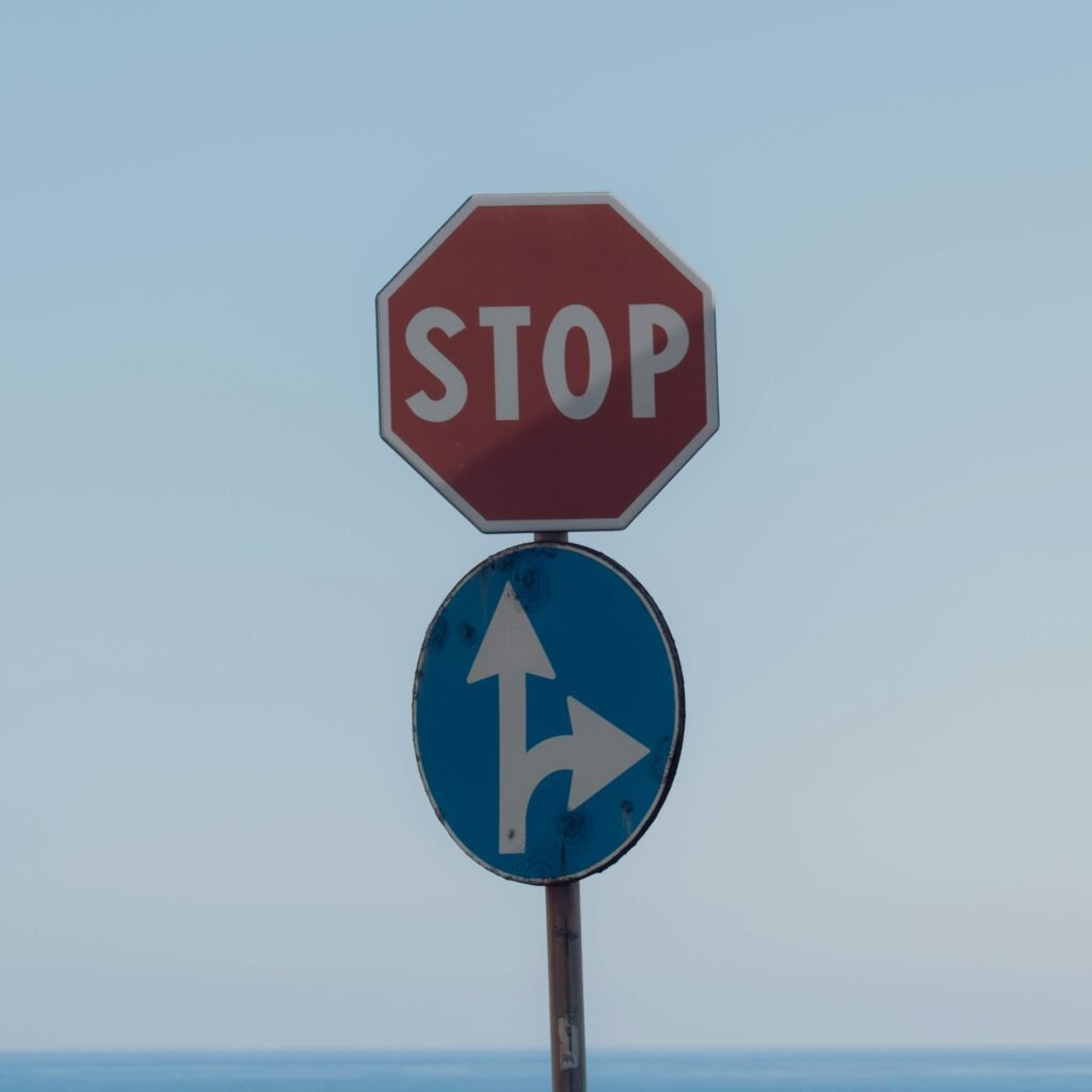 Stop sign with directional arrows at Lido di Noto, Sicily with sky backdrop.