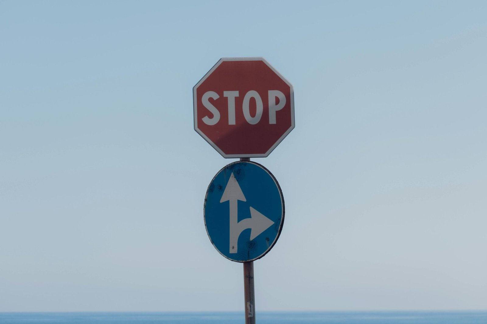 Stop sign with directional arrows at Lido di Noto, Sicily with sky backdrop.