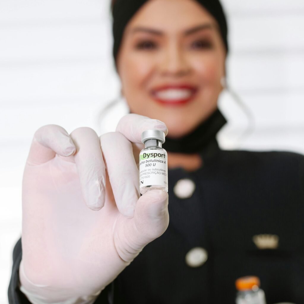 A healthcare worker in gloves holding a Dysport vial, smiling indoors.