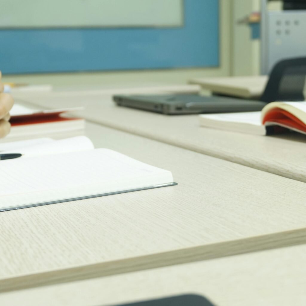 Close-up of a professional meeting setup with hands, laptops, and notebooks on a wooden desk.