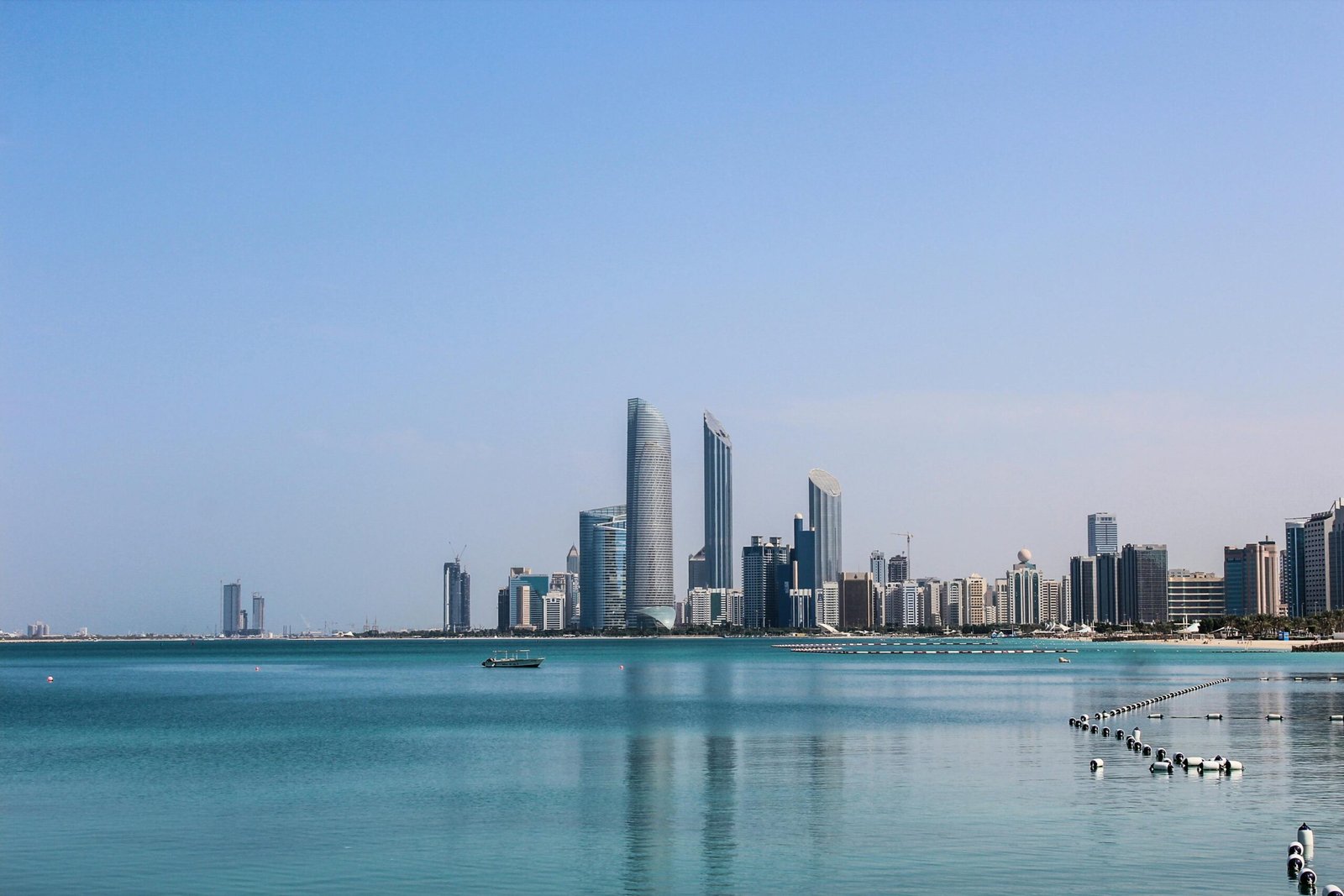 Stunning view of the Abu Dhabi skyline reflecting in the calm Gulf waters on a sunny day.
