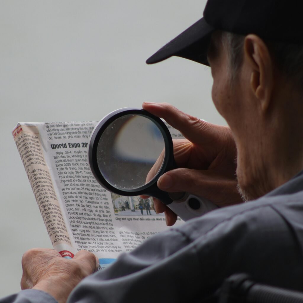 Elderly man using a magnifying glass to enhance text in a newspaper.