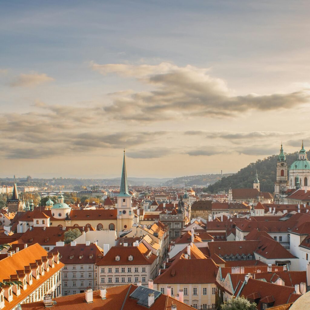 Captivating view of Prague's historic skyline with red rooftops and iconic architecture under a warm sunset.