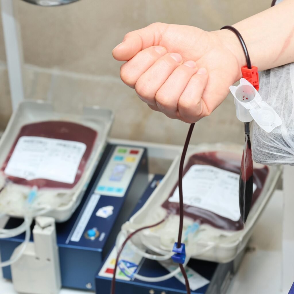 Close-up of blood donation process showing a donor's arm and blood bags in a clinic.