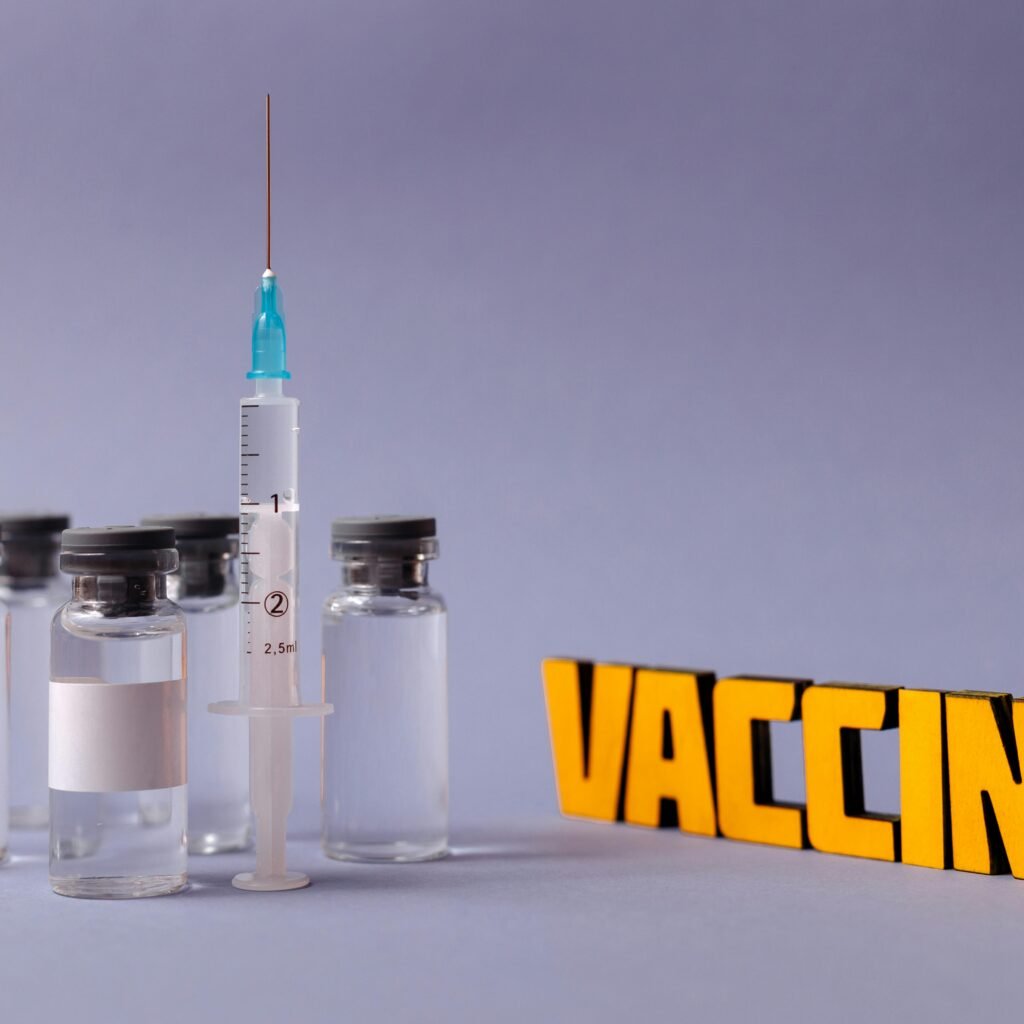 Syringe and vaccine vials with 'vaccine' text on a gray background, representing vaccination efforts.