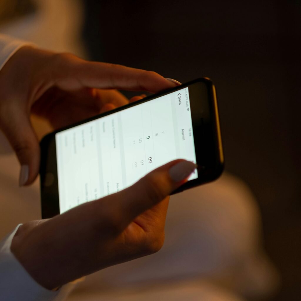 Close-up of hands setting an alarm on a smartphone, depicting night usage and technology interaction.