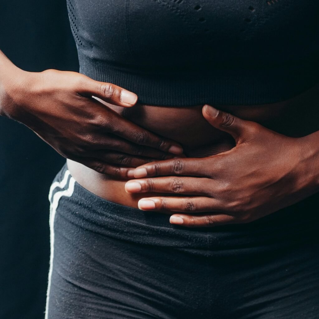 Close-up of a person pressing hands on abdomen, indicating discomfort or pain, against a black background.