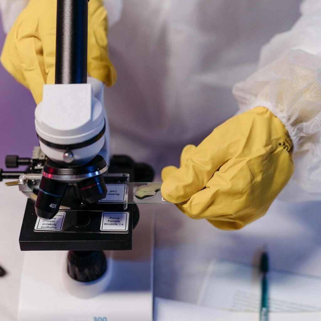 Researcher in protective gloves examines samples under a microscope in a lab setting.