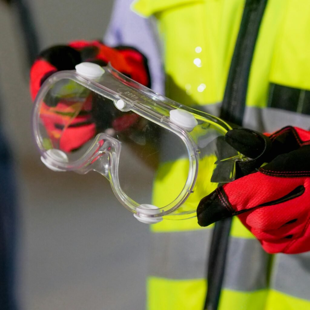 Close-up of a person holding safety goggles with protective gloves, featuring high visibility gear.