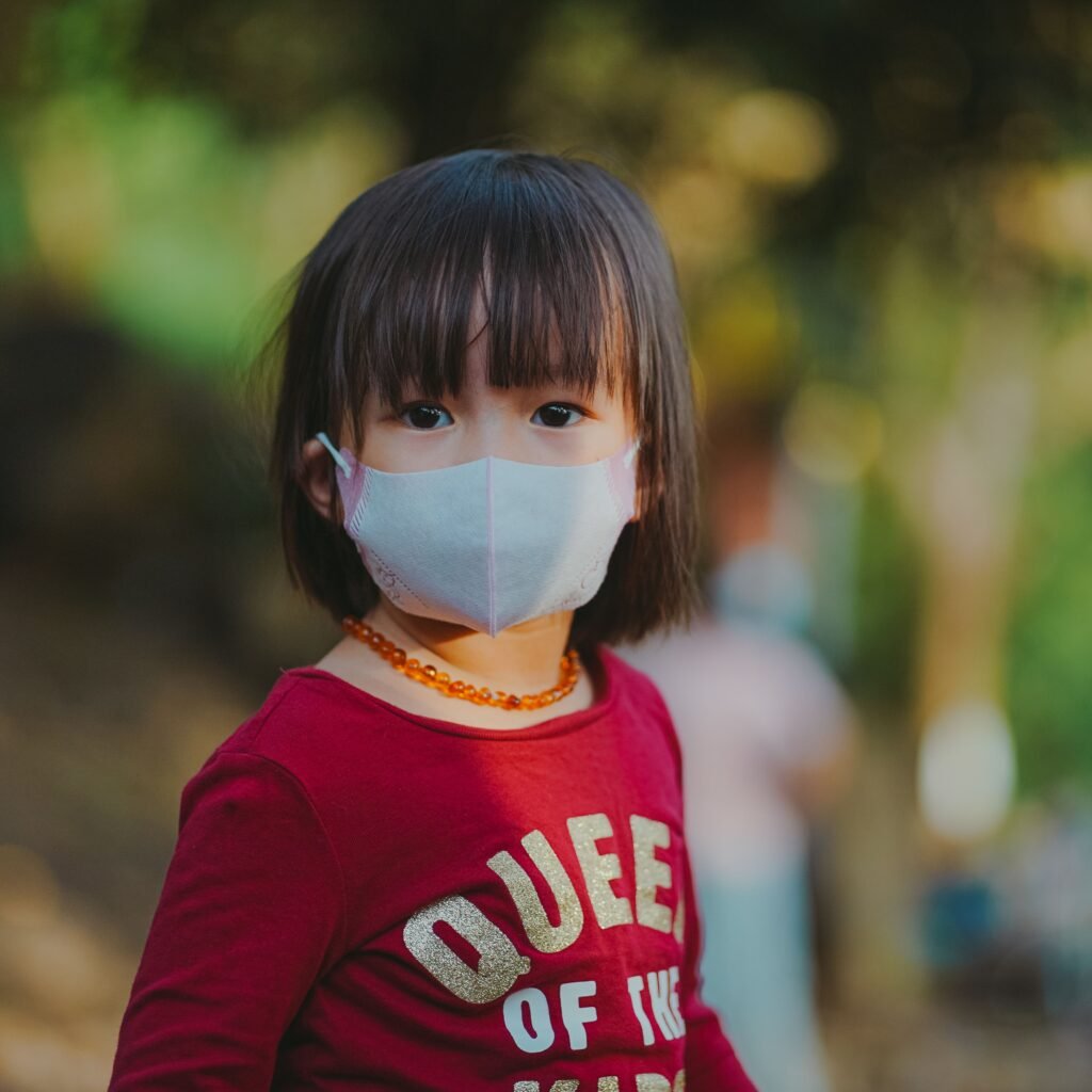 Adorable young girl wearing a face mask outdoors, emphasizing protection during pandemic.