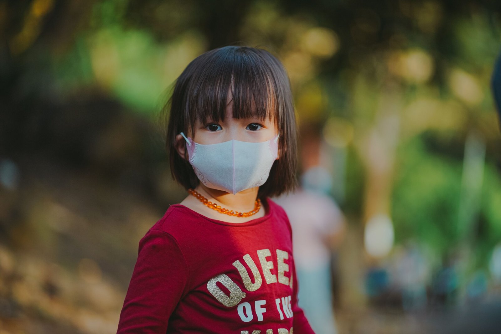 Adorable young girl wearing a face mask outdoors, emphasizing protection during pandemic.