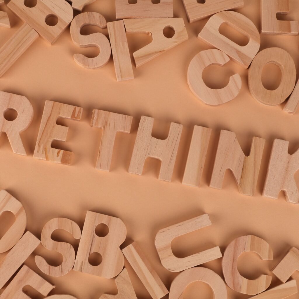 Wooden alphabet letters forming the word rethink on a flat, peach-colored background.