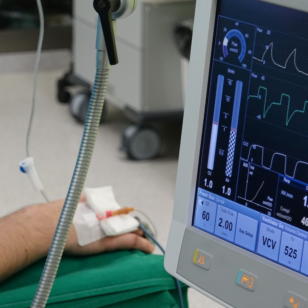 A close-up of a patient's hand connected to medical equipment in an ICU room.