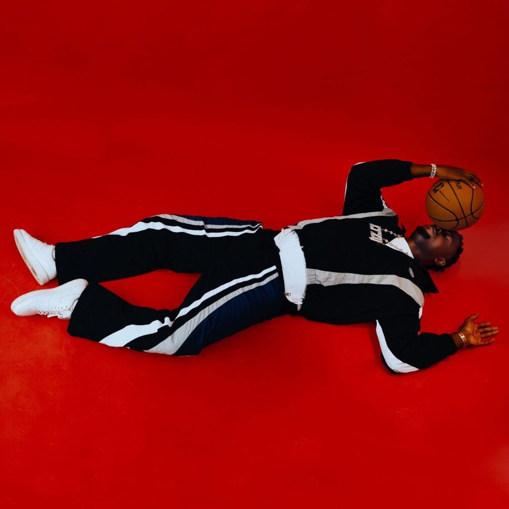 Stylish man in streetwear lies on red floor holding a basketball, exuding urban cool.