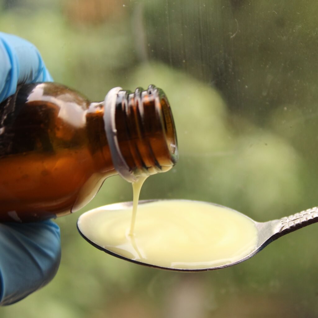 Close-up of liquid medicine being poured into a spoon, captured with gloves for medical use.