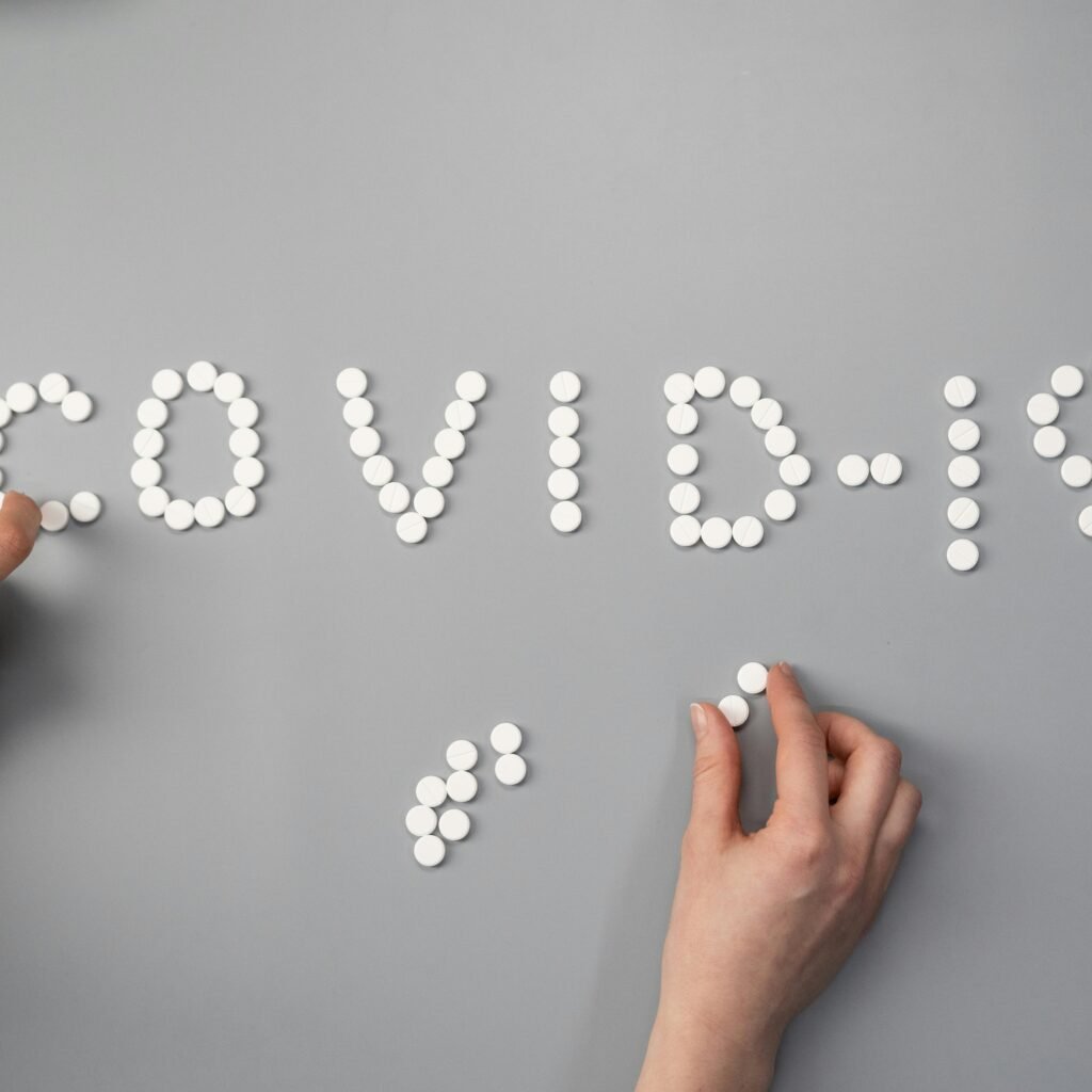 Hands arranging white pills to spell 'COVID-19' on a gray surface, symbolizing medical and health themes.