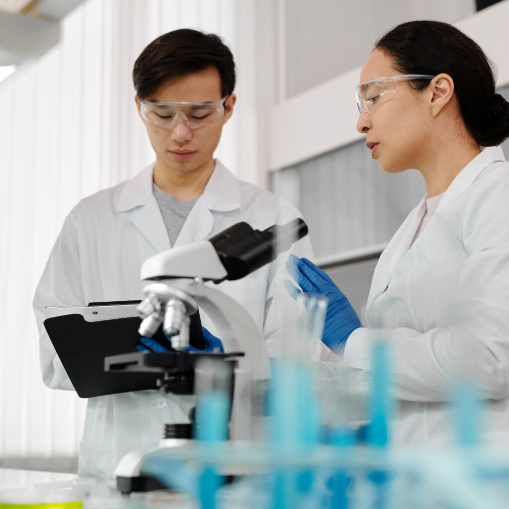 Asian scientists in lab coats discussing research with a microscope in a laboratory setting.