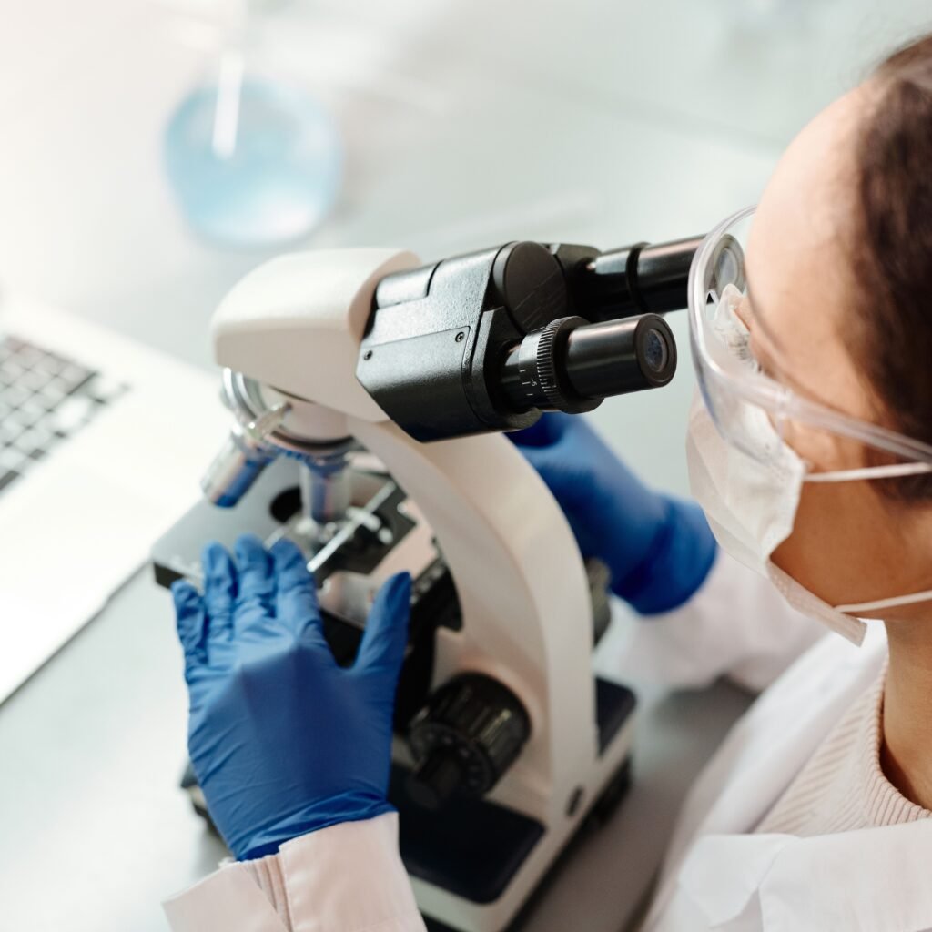 Scientist in protective gear examining samples with microscope in laboratory setting.