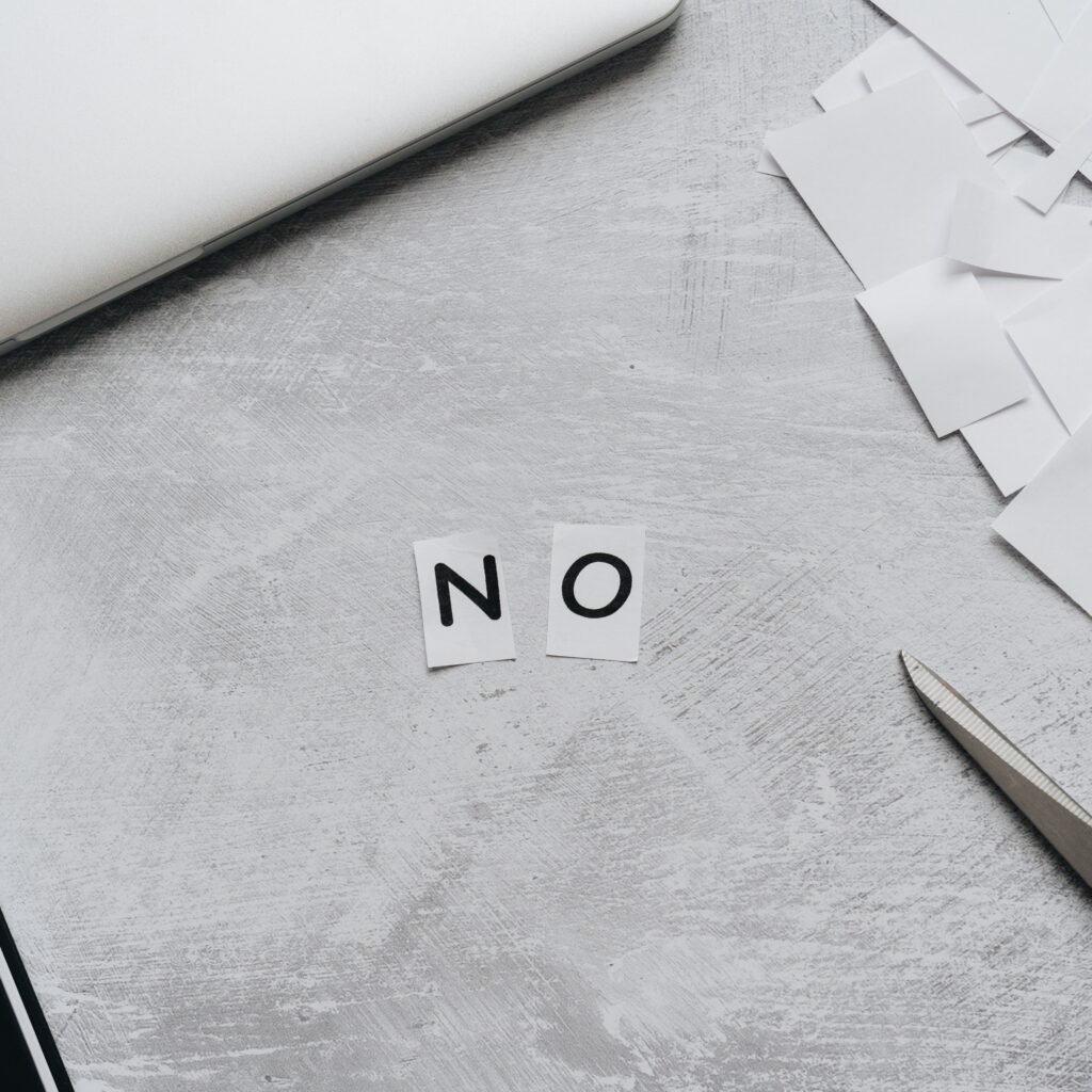 Top view of scattered paper squares, laptop, and scissors forming the word 'NO', implying rejection or denial.