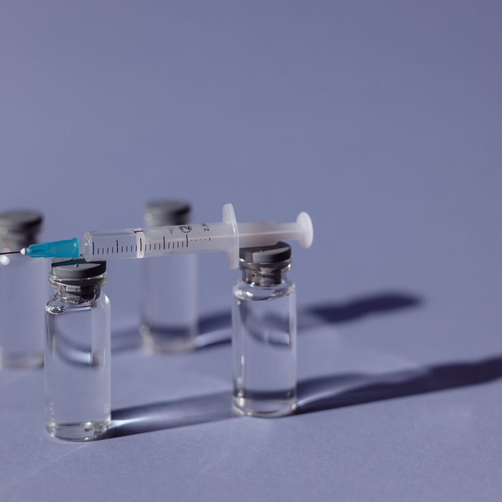 A syringe balanced on vaccine vials with a purple backdrop, representing medical treatment.