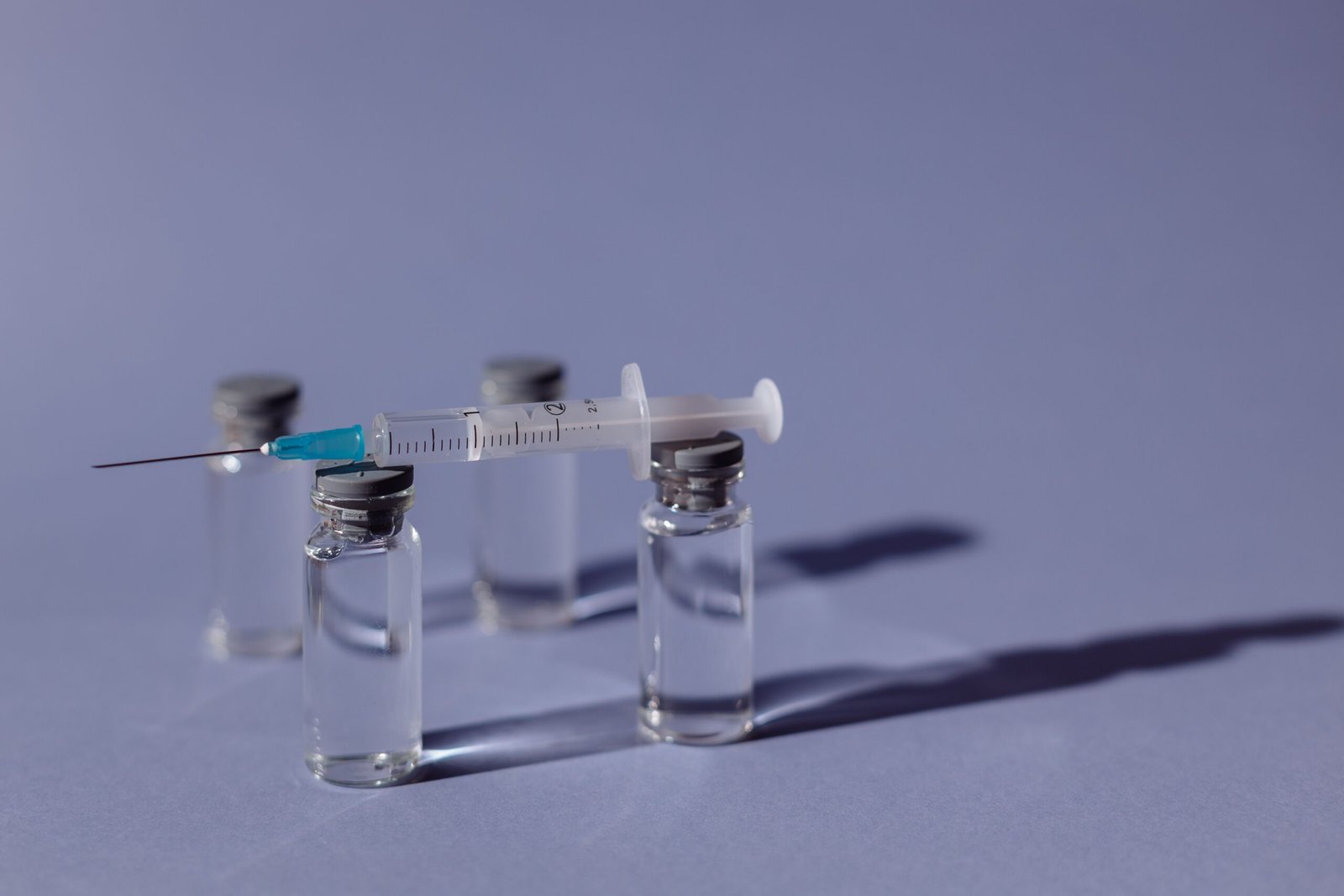 A syringe balanced on vaccine vials with a purple backdrop, representing medical treatment.