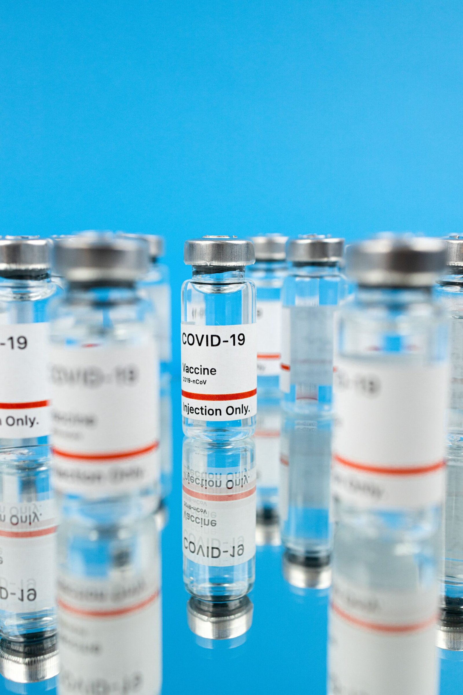 Close-up of COVID-19 vaccine vials on a reflective surface against a blue background.