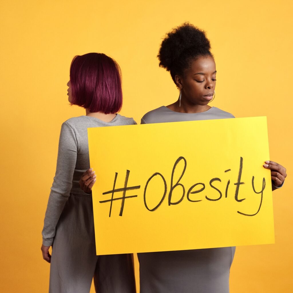 Two women advocate obesity awareness holding a bold sign with a vibrant yellow backdrop.